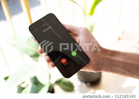 Fraud or fraudulent schemes. Close-up of a male hand holding a phone with an unexpected incoming call from an unknown 112165143