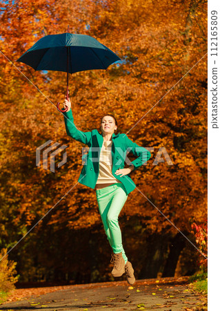 Woman jumping with umbrella in park during autumn 112165809
