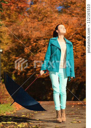 Girl walking with blue umbrella in autumnal park 112165810