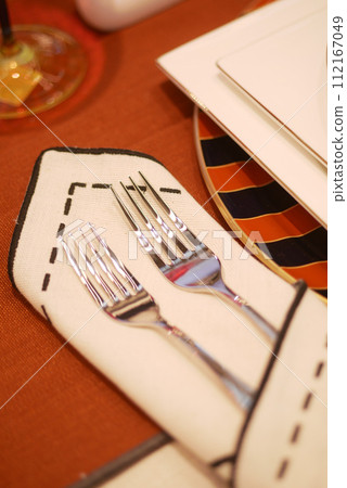 Two forks displayed on a wooden table with a napkin underneath 112167049
