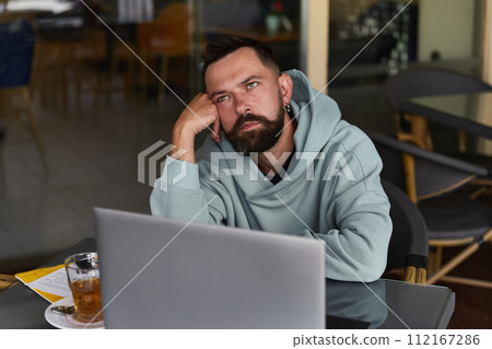 Pensive bearded man in casual clothes in cafe using his laptop 112167286