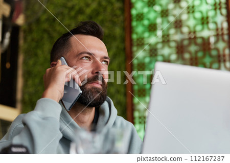 Cheerful young adult man in casual clothes in cafe talking on a mobile phone 112167287