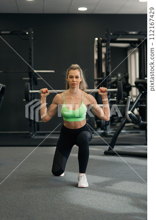 Young woman does dumbbell lunges in gym Young woman does dumbbell lunges in gym 112167429