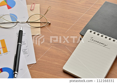 A desk with a notepad that says Taxonomy, glasses and a pen 112168331