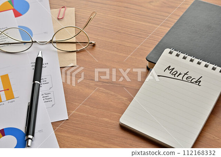 A desk with a notepad that says Martech, glasses, and a pen A desk with a notepad that says Martech, glasses, and a pen 112168332