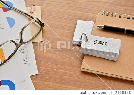 一張桌子，上面有一本寫有 SEM 的詞彙書、眼鏡和一支筆 112168338