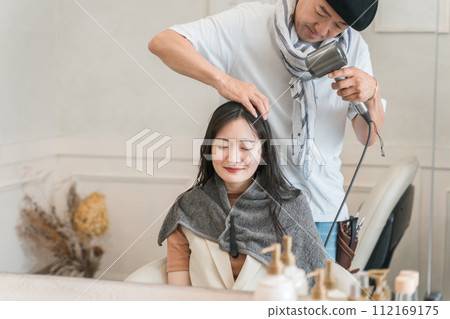 Stylist/hairdresser and female customer drying hair with a hair dryer 112169175