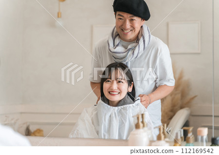 一名男性造型師/美容師在美容院為女性顧客提供服務 一名男性造型師/美容師在美容院為女性顧客提供服務 112169542