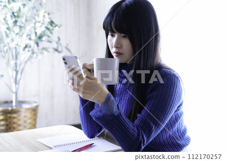 一位女士在學習時用智慧型手機和咖啡休息一下 112170257