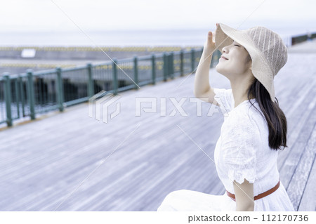 A woman in a white dress relaxing on the wooden deck of a marina 112170736