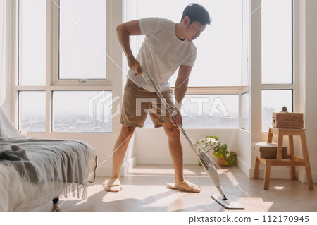 Asian Thai man using mop for cleaning floor in living room apartment, Man do household chores, housework concept. Asian Thai man using mop for cleaning floor in living room apartment, Man do household chores, housework concept. 112170945