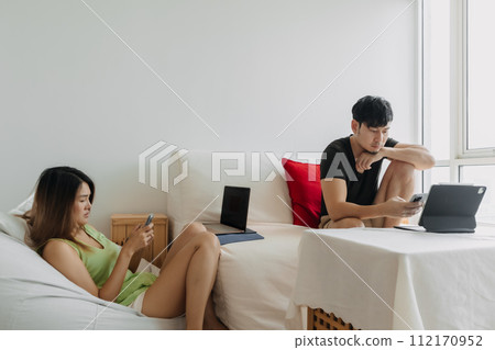 Asian Thai couple using laptop, Both man and woman busy working on notebook, lover freelancer sitting on couch in room apartment. Asian Thai couple using laptop, Both man and woman busy working on notebook, lover freelancer sitting on couch in room apartment. 112170952