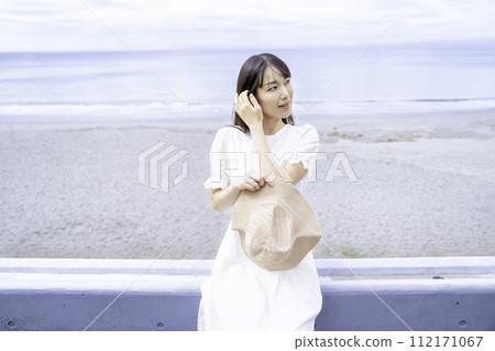 A woman in a white dress strolling by the sea 112171067