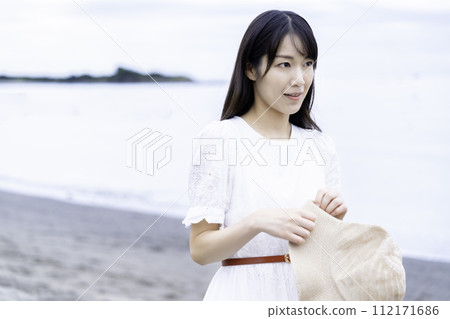 A woman in a white dress strolling by the sea 112171686
