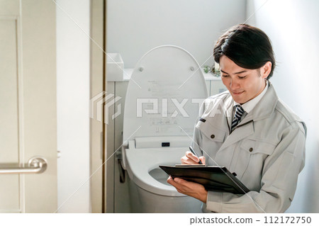 A male businessman at an equipment shop/plumbing shop in work clothes checking the toilet 112172750