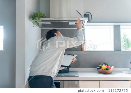 A male businessman in work clothes inspects the range hood and ventilation fan in the kitchen. A male businessman in work clothes inspects the range hood and ventilation fan in the kitchen. 112172755