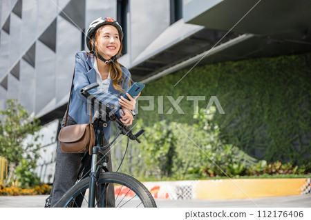 Eco friendly, Lifestyle business female using bike outdoor in morning, Asian smiling young woman with helmet hold mobile smart phone talk with business during go to office work at street with bicycle 112176406