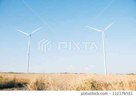 The picturesque scene of wind turbines on a mountain farm spinning in harmony with nature. Clean energy technology against a blue sky embracing sustainable development. The picturesque scene of wind turbines on a mountain farm spinning in harmony with nature. Clean energy technology against a blue sky embracing sustainable development. 112176581