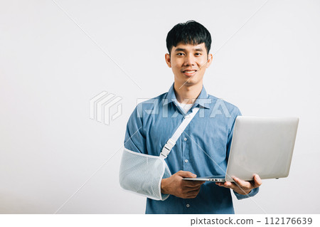 An Asian businessman, despite a broken arm, maintains confidence, using a splint for treatment while working on a laptop. Studio shot isolated on white background, emphasizing dedication and recovery. 112176639