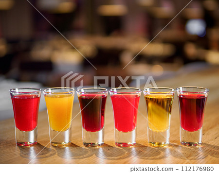 Set of colorful different bitters and liqueurs in shot glasses on bar counter. Collection of shooters. Selection of natural berry alcoholic tinctures in glasses. Different bitters and liqueurs Set of colorful different bitters and liqueurs in shot glasses on bar counter. Collection of shooters. Selection of natural berry alcoholic tinctures in glasses. Different bitters and liqueurs 112176980