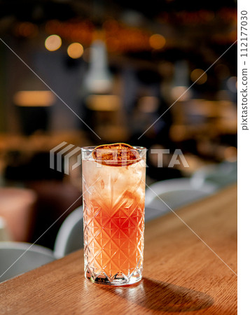 Glass of frozen citrus cocktail with triple sec on bar counter in restaurant interior background, copy space Glass of frozen citrus cocktail with triple sec on bar counter in restaurant interior background, copy space 112177030