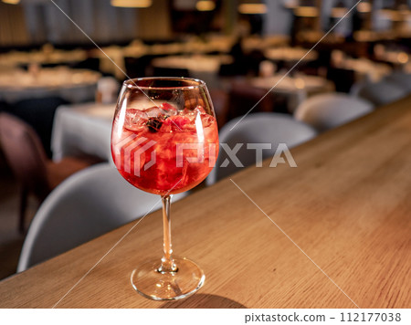 Glass of orange aperol spritz cocktail. Aperitif pink cocktail in wine glass with sparkling wine, syrup and ice cubes on bar counter in restaurant interior background, copy space Glass of orange aperol spritz cocktail. Aperitif pink cocktail in wine glass with sparkling wine, syrup and ice cubes on bar counter in restaurant interior background, copy space 112177038