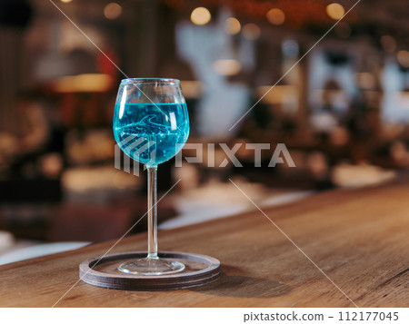 Glass of blue lagoon cocktail in shark high stem cocktail glass on beautiful bar counter background with copyspace. Aesthetic photo of blue lagoon cocktail in evening light, restaurant or bar interior 112177045