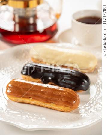 Group of french dessert Eclair on white plate. Caramel, chocolate and vanilla glazed eclairs on white plate in restaurant table background. Perfect french eclairs set Group of french dessert Eclair on white plate. Caramel, chocolate and vanilla glazed eclairs on white plate in restaurant table background. Perfect french eclairs set 112177091
