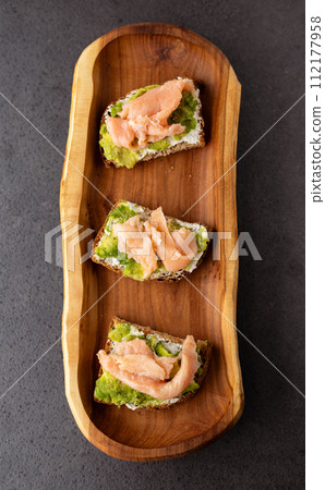 toast with cream cheese, avocado and salmon on a wooden plate, dark background 112177958
