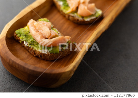 toast with cream cheese, avocado and salmon on a wooden plate, dark background 112177960