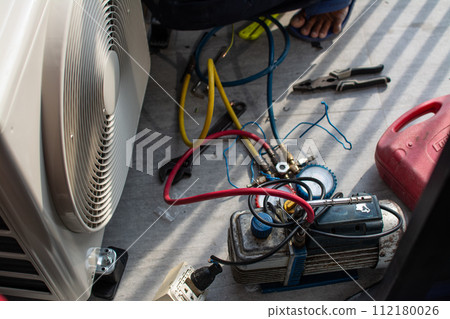 Air conditioning, HVAC service technician using gauges to check refrigerant and add refrigerant outdoor compressor unit. 112180026