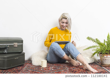 Woman in yellow reads tablet beside vintage suitcase. Woman in yellow reads tablet beside vintage suitcase. 112180141