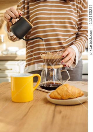 female makes coffee in morning kitchen. brews in purover. yellow cup with black coffee drip 112180233