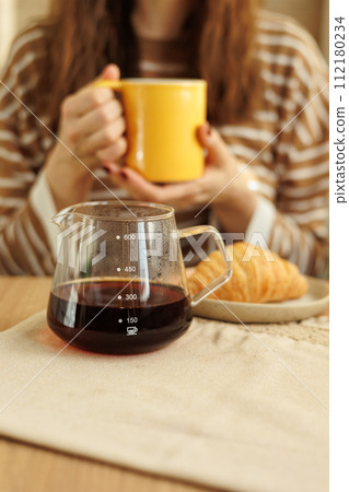 female makes coffee in morning kitchen. brews in purover. yellow cup with black coffee drip 112180234
