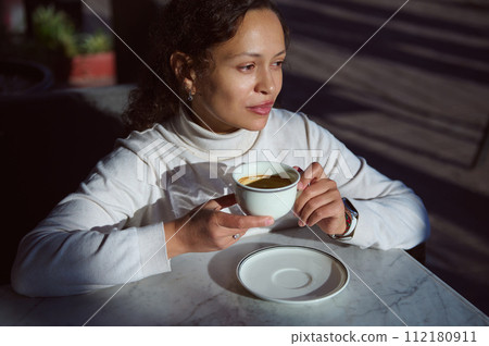 Authentic portrait of young beautiful Latin American woman with a cup of coffee in a coffee shop in the sunny day 112180911