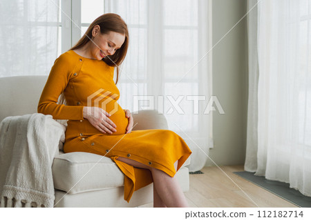 Pregnancy motherhood people expectation future. Pregnant woman with big belly sitting on chair near window at home. Girl hugging her tummy enjoying pregnancy. Maternity tenderness parenthood new life Pregnancy motherhood people expectation future. Pregnant woman with big belly sitting on chair near window at home. Girl hugging her tummy enjoying pregnancy. Maternity tenderness parenthood new life 112182714