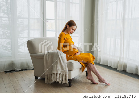 Pregnancy motherhood people expectation future. Pregnant woman with big belly sitting on chair near window at home. Girl hugging her tummy enjoying pregnancy. Maternity tenderness parenthood new life Pregnancy motherhood people expectation future. Pregnant woman with big belly sitting on chair near window at home. Girl hugging her tummy enjoying pregnancy. Maternity tenderness parenthood new life 112182719