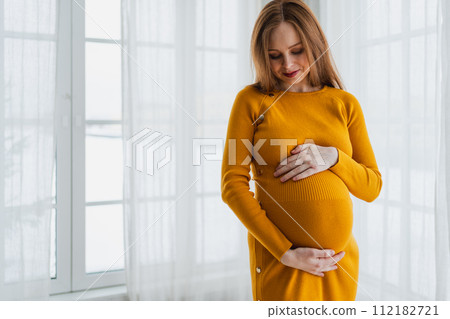 Pregnancy motherhood people expectation future. Pregnant woman with big belly standing near window at home. Girl hugging her tummy enjoying pregnancy. Maternity tenderness parenthood new life concept Pregnancy motherhood people expectation future. Pregnant woman with big belly standing near window at home. Girl hugging her tummy enjoying pregnancy. Maternity tenderness parenthood new life concept 112182721