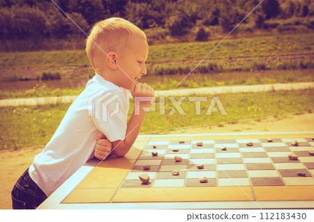Little boy clever child playing checkers in park Little boy clever child playing checkers in park 112183430
