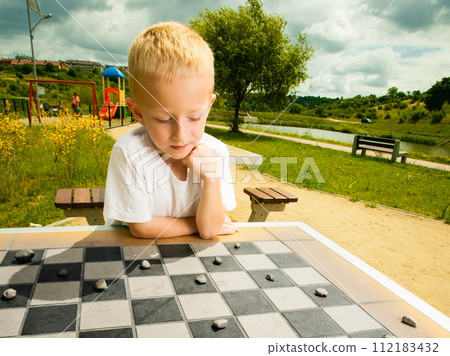 Child playing draughts or checkers board game outdoor 112183432