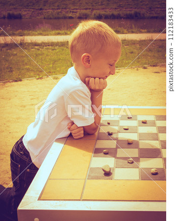 Little boy clever child playing checkers in park 112183433