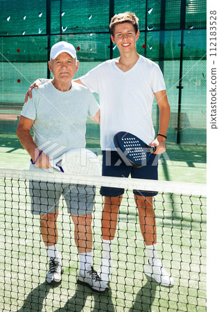 Senior man and young man posing on padel court Senior man and young man posing on padel court 112183528
