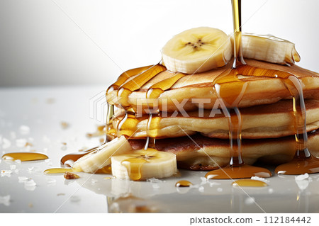 Stack of pancakes with maple syrup and banana slices on top. 112184442