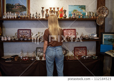 A young blonde woman chooses souvenirs in a shop in the Old Town. Tourism concept. A young blonde woman chooses souvenirs in a shop in the Old Town. Tourism concept. 112184523
