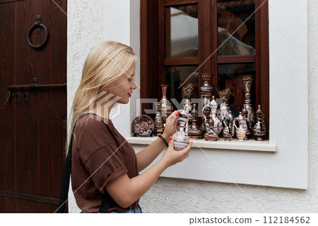 A young blonde woman looks at a souvenir at a street market in the Old Town. 112184562