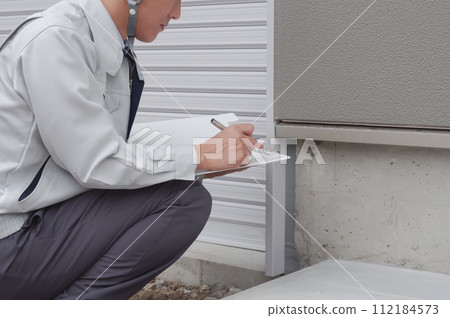 A man inspecting the foundation of a house A man inspecting the foundation of a house 112184573