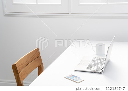 Laptop, smartphone and mug on a white table by the window 112184747