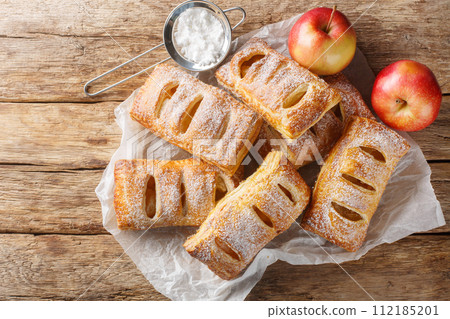 Freshly baked apple puff pastries with powdered sugar close-up on a paper. Horizontal top view Freshly baked apple puff pastries with powdered sugar close-up on a paper. Horizontal top view 112185201