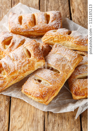 Danish apple puff pastry covered with powdered sugar close-up. Vertical Danish apple puff pastry covered with powdered sugar close-up. Vertical 112185213