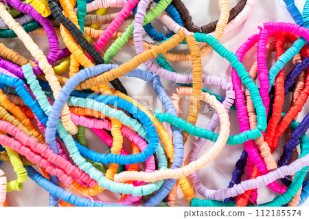 A vibrant collection of clay beads, neatly arranged by color on a white table, ready to inspire young crafters to create their own unique bracelets. A vibrant collection of clay beads, neatly arranged by color on a white table, ready to inspire young crafters to create their own unique bracelets. 112185574